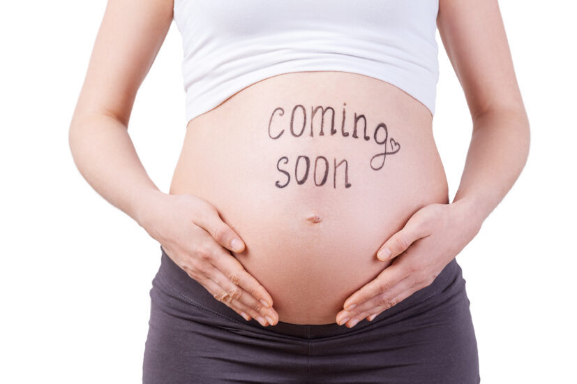Coming soon. Cropped image of pregnant woman with coming soon sign on her belly standing isolated on white